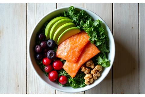 Overhead shot of a colorful salad rich in omega-3s and antioxidants (salmon, avocado, walnuts, leafy greens) on a light wooden background, symbolizing cognitive health.